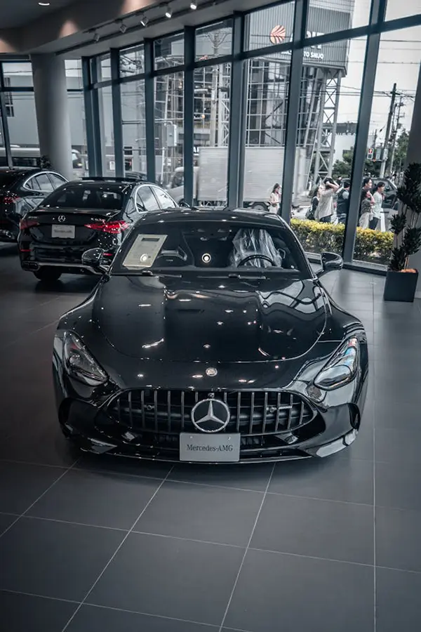 Black Mercedes-AMG car prominently displayed in a luxury showroom with tiled floors, large windows, and an urban street view in the background, highlighting its high-performance design.