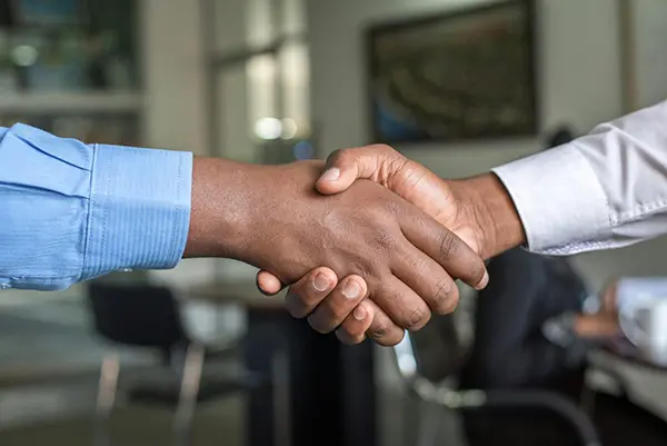 Close-up of a handshake between two individuals wearing formal attire in a professional office setting, symbolizing partnership and agreement.