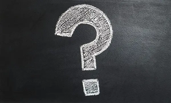 Large textured white question mark drawn in chalk on a dark chalkboard-like background, representing a focus on curiosity and problem-solving.
