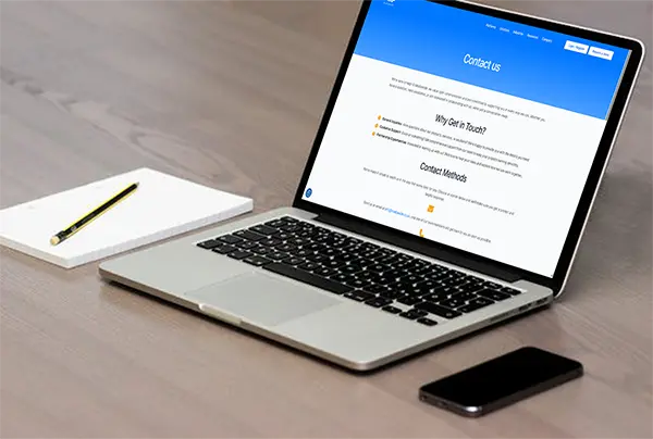 Professional workspace featuring a laptop displaying a Contact Us webpage with options for inquiries, customer support, and partnerships, alongside a notebook and smartphone on a wooden desk.