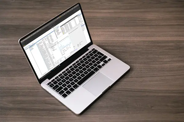 Laptop on a wooden surface displaying multiple windows and a line chart, representing a data analysis or management workspace in a professional or educational context.