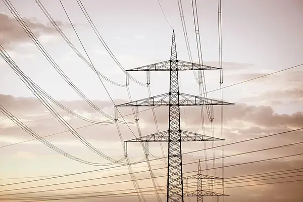 Silhouetted electrical transmission towers and power lines set against a warm gradient sky, showcasing energy infrastructure and distribution systems.