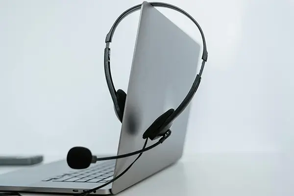 Silver laptop with a black headset draped over its screen, set against a plain white background, symbolizing remote work and virtual communication.