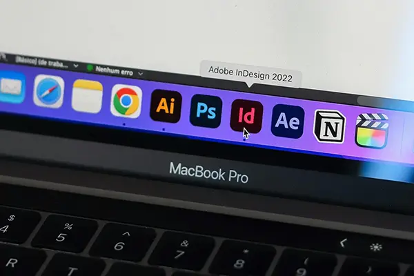 Close-up of a MacBook Pro dock with application icons, including Adobe Creative Cloud tools. The cursor is hovering over the Adobe InDesign icon with a tooltip displaying Adobe InDesign 2022.