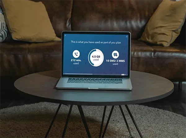 Laptop on a round table displaying a mobile plan usage summary with 212 minutes used, 4.5 GB of data, and 10 SMS/2 MMS sent, set in a cozy home setting for easy digital plan management.