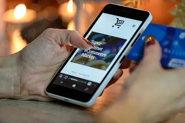 A person holding a smartphone displaying an eCommerce website and a blue credit card, with a warm-lit background, showcasing the convenience of online shopping and secure digital payments.