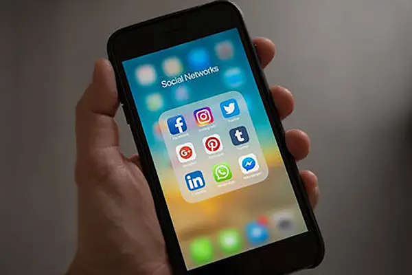 Smartphone screen with a 3x3 grid of social media app icons, including Facebook, Instagram, Twitter, and WhatsApp, against a gradient blue-to-green background.