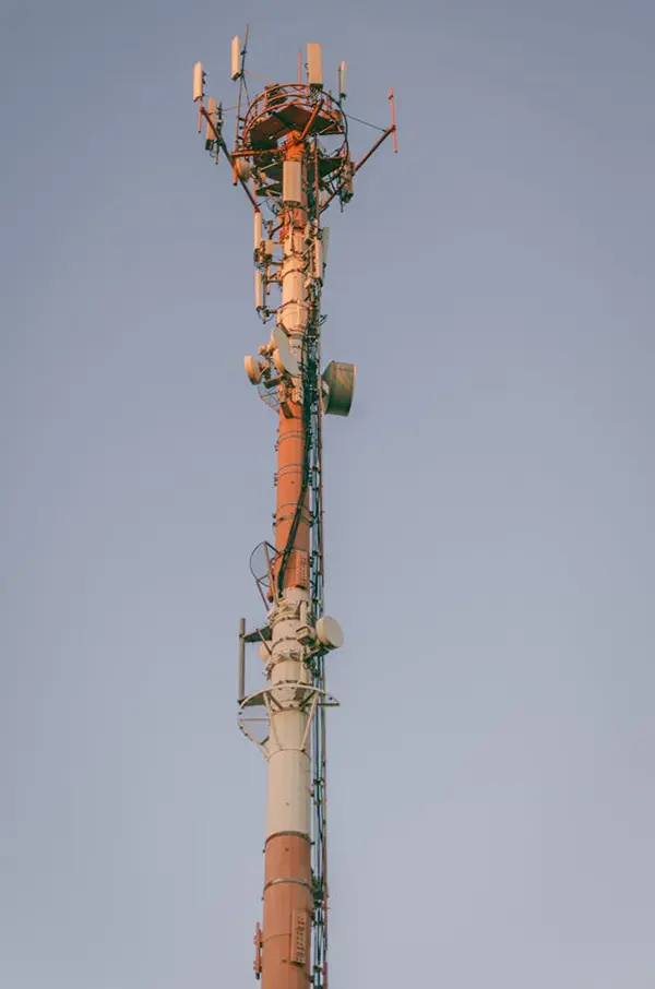 Red and white telecommunications tower with antennas and a satellite dish extending vertically against a clear blue sky, serving as critical infrastructure for signal transmission and broadcasting.