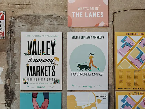 A collection of posters promoting the Valley Laneway Markets, detailing event dates, a dog-friendly environment, and a colorful map of the market area, creating an inviting community-focused display.